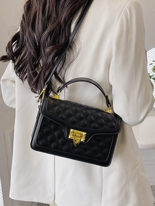 Sac à bandoulière matelassé noir avec fermoir doré sur fond de costume blanc