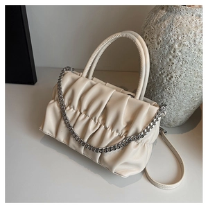 Detail of a creamy white pleated cloud bag with silver chain and leather strap on a table