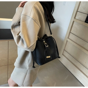 Detail of black lychee grain leather bucket bag with gold hardware on a beige outfit