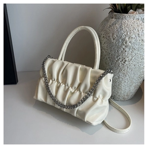 Detail of ruched cream leather handbag with silver chain on a decorative white pedestal