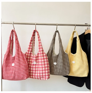 Detail view of colorful plaid canvas tote bags with leather labels hanging on a metal rack