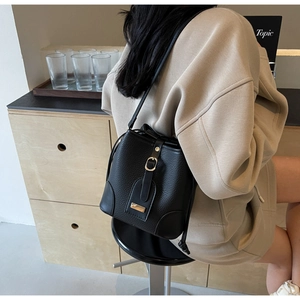 Detail of black lychee grain leather bucket bag featuring gold hardware and drawstring