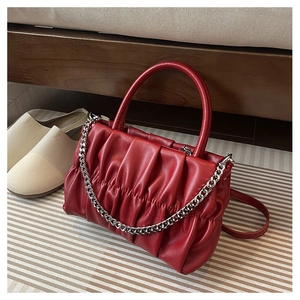 Close-up of a red pleated cloud bag with silver chain and thin strap on a rug