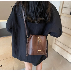 Rear view of model wearing a brown lychee-patterned bucket bag with a golden buckle