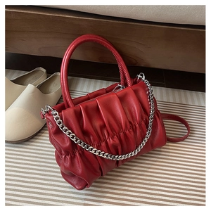 Macro detail of red ruched leather handbag with metal chain and curved handle