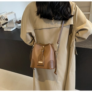 Brown lychee leather bucket bag with drawstring closure worn by model in a cafe