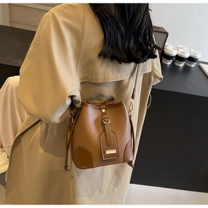 Detail of a brown lychee pattern leather bucket bag with drawstring on a trench coat