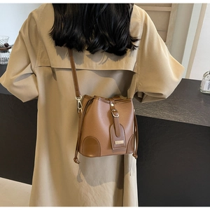 Brown litchi leather bucket bag shown on a model wearing a classic khaki trench coat