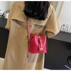 Detail of red pebbled leather bucket bag with metal lock worn as a crossbody by model