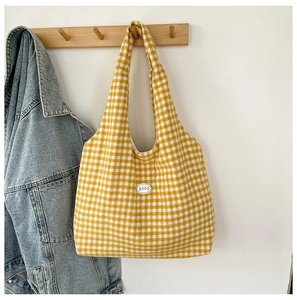 Detail of a yellow and white gingham tote bag with a 'good' patch on a wall hook