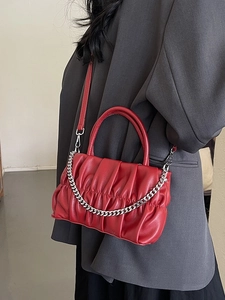 Deep red pleated crossbody bag with silver chain worn over a grey blazer jacket