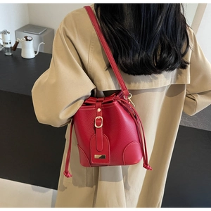 Red bucket bag with drawstring closure and gold buckle shown on a model in trench coat