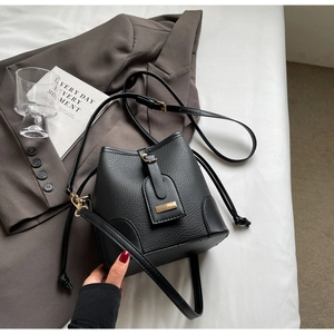 Top view of black pebbled leather bucket bag with gold hardware on a grey blazer