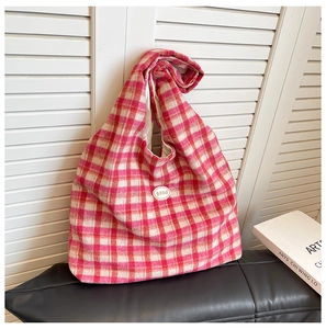 Detail of pink and cream checkered tweed tote bag with circular logo on wooden backdrop