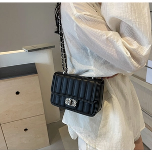 Close-up of black quilted crossbody bag with diamond-studded twist lock and chain strap