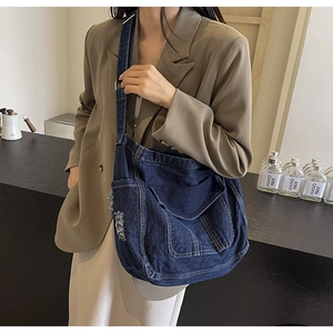 Detail of blue denim crossbody bag featuring distressed edges and large front flap pocket