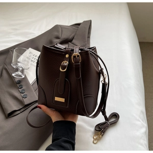 Detailed view of dark brown litchi grain leather bucket bag with gold metal buckle
