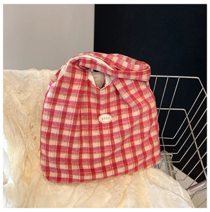 Detail of red and white checkered tote bag with oval Good logo label on lace background