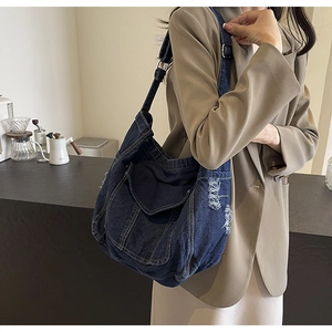 Detail of dark blue denim tote bag featuring distressed frayed edges and adjustable strap