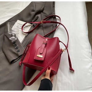 Close-up of red litchi texture bucket bag with metal buckle on a grey blazer background