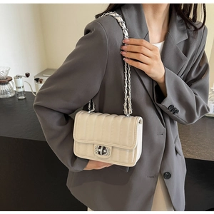 Detail of light beige quilted crossbody bag with rhinestone buckle and silver chain