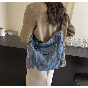 Detail of blue denim crossbody bag with large side pockets and distressed frayed edges
