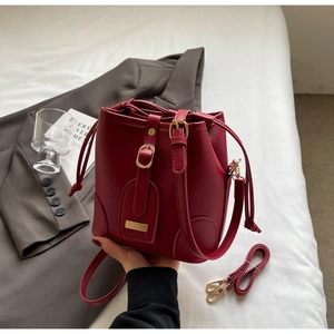 Detail of burgundy bucket bag with litchi texture leather and gold metal hardware