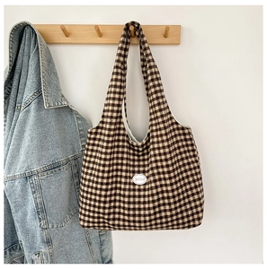 Detail view of large tote bag in brown and black checkered canvas with a small round logo