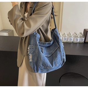 Detail shot of distressed dark blue denim hobo bag featuring frayed holes and side pockets