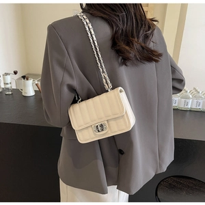 Detail of ivory quilted crossbody bag with silver rhinestone lock on a cafe table