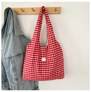 Detail of red and white checkered canvas tote bag with a 'good' patch hanging on a hook