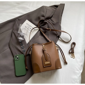 Detailed view of a brown pebbled leather bucket bag with drawstring and golden buckle