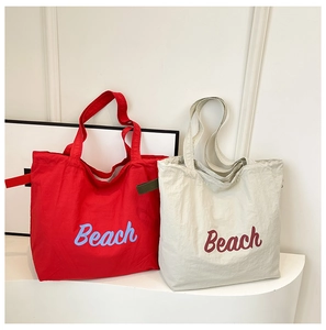 Detalle de bolsos tote de nailon rojo y gris claro con estampado Beach y ganchos de cincha