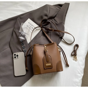Detail of brown litchi pattern bucket bag with drawstring closure and metal buckle hardware