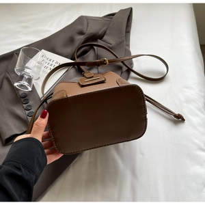 Detail of brown litchi pattern leather bucket bag with metal buckle on white bedding