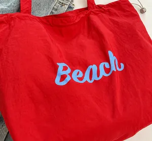 Detalle de bolso tote de nailon rojo con letras Beach azules y cordón de ajuste