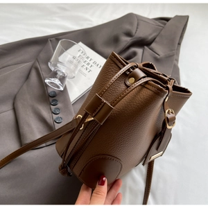 Close-up of brown lychee-grain leather bucket bag with drawstring and golden hardware