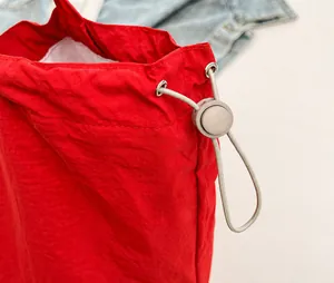 Detalle del bolso de nailon rojo con cordón, ojales metálicos y hebilla de resorte ajustable