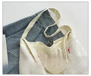 Dettaglio della borsa tote in velluto a coste bianco con lettere ricamate e tracolle larghe
