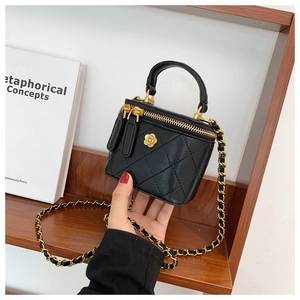 Detalle de bolso cubo acolchado negro con camelia dorada y correa de cadena chic