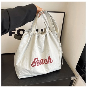 Detalle de bolso tote de nailon gris claro con letras Beach rojas y cierre de cordón
