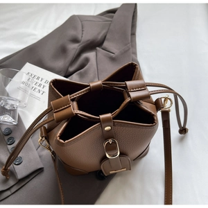 Detail of brown litchi pattern leather bucket bag with metal buckle and drawstring closure