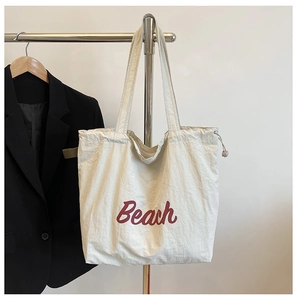 Detalle del bolso tote de nailon blanco roto con letras Beach rojas y cierre de cordón