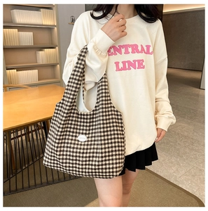 Close-up of a checkered canvas tote bag worn with a casual sweatshirt in a warm interior