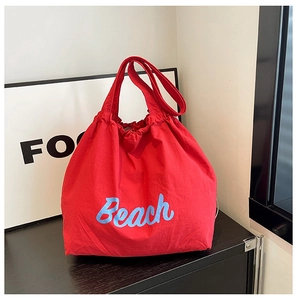 Detalle del bolso tote rojo de nailon con texto Beach azul claro sobre fondo negro