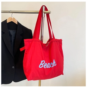 Detalle del bolso tote de nailon rojo con letras Beach azules en una elegante pantalla