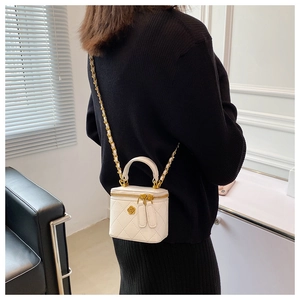 Detalle de bolso tipo cubo acolchado blanco con cadena dorada llevado por una modelo