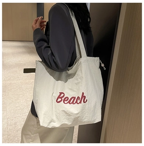 Detalle del bolso tote de lona blanco roto con texto Beach rojo y cierre de cordón
