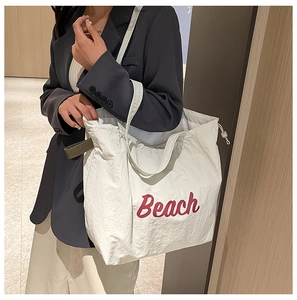 Detalle de un bolso tote de nailon crema con texto Beach rojo llevado por mujer