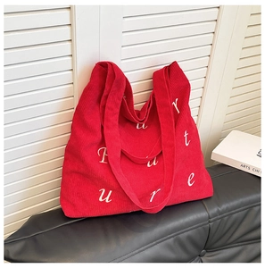 Dettaglio borsa shopper in velluto a coste rosso con ricamo su panca in pelle nera